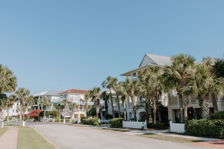 Row of elevated Gulf Coast homes lined with palm trees under a clear blue sky