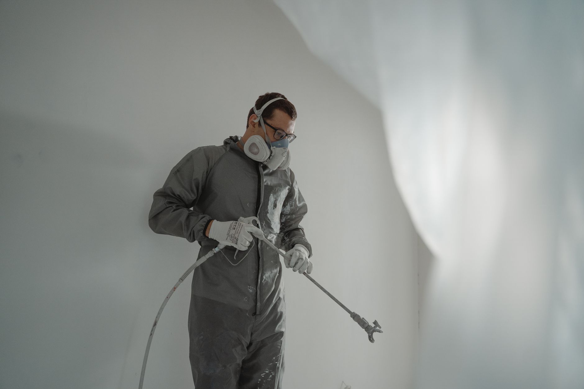 Insulation technician in protective suit and respirator spraying foam onto an interior wall